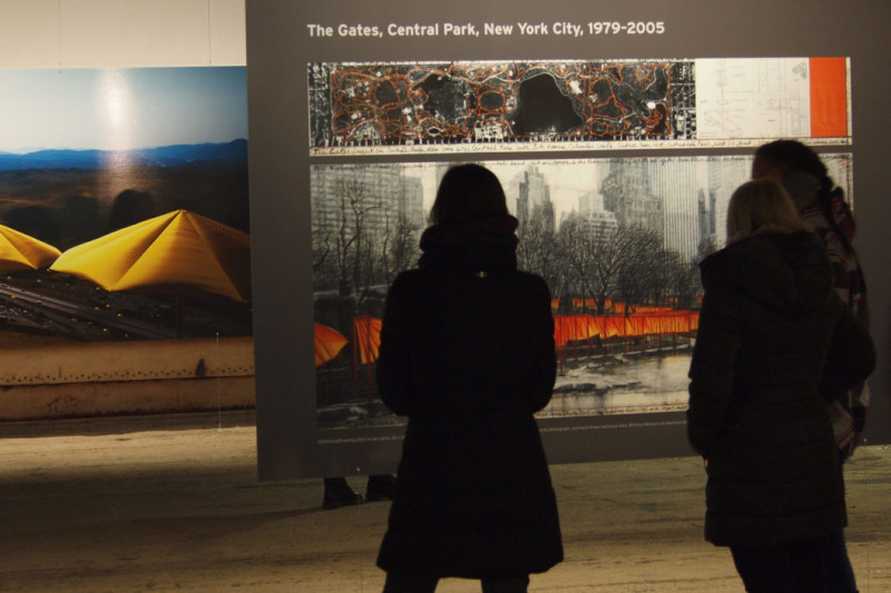 Foto zwei im Vordergrund stehender Personen beim Betrachten von einer großen grauen Tafel mit Fotos.