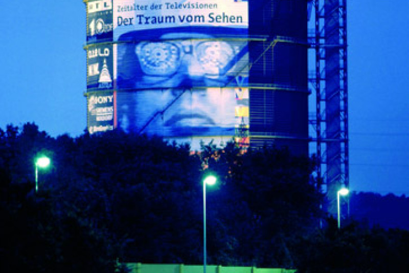 Fotografie vom Gasometer am Abend mit dem Plakat der Ausstellung der Traum vom Sehen.