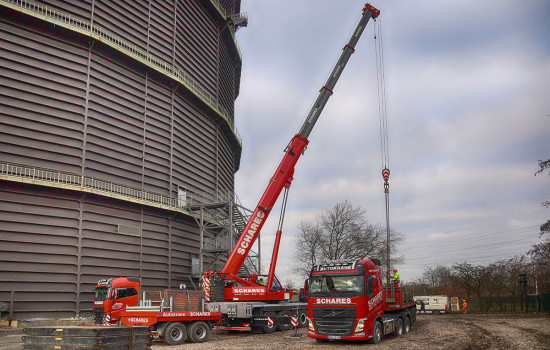 Ein roter Autokran entlädt Bauteile von einem weiteren LKW.