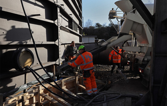 Drei Arbeiter füllen Beton aus einem Betonmischer in die Verschalung für das Fundament des Gasometers.
